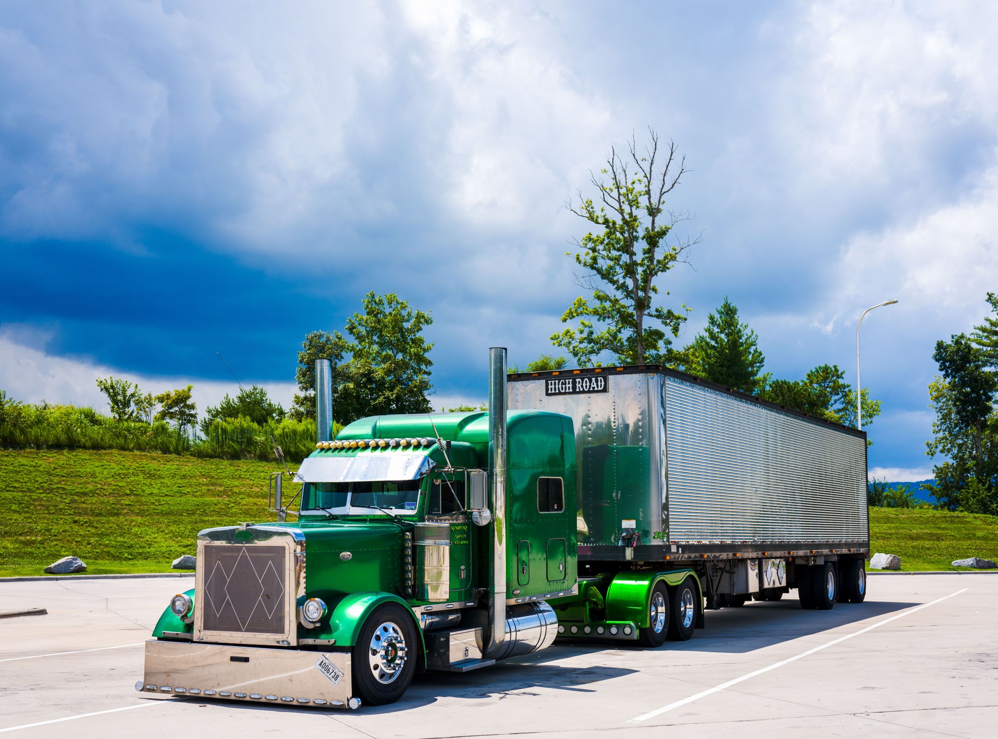 Green American semi truck and trailer parked beside a landscaped roadway
